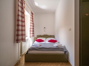 A narrow room with a bed, a radiator, and a door with a heart-shaped decoration. - Apartment House Berghi Ii (Kranjska Gora)