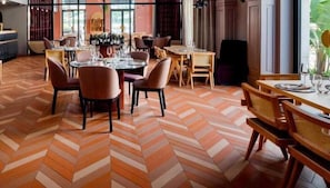 A restaurant with a herringbone patterned floor, wooden tables and chairs, and a bar area with bottles. - Koper (Koper)
