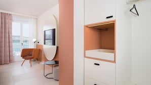 Ett modernt hotellrum med en stor garderob, en sittgrupp med en stol och ett bord samt utsikt genom fönstret.