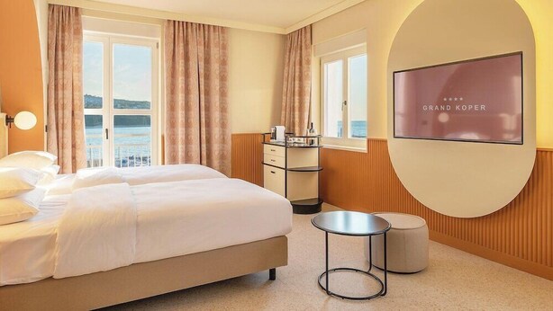 Ett hotellrum med en säng, ett litet bord, en stol, en tv och utsikt över havet.