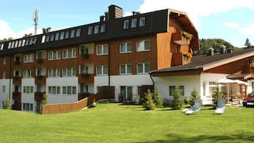A multi-story residential building with balconies, a grassy yard, and a car parked outside.