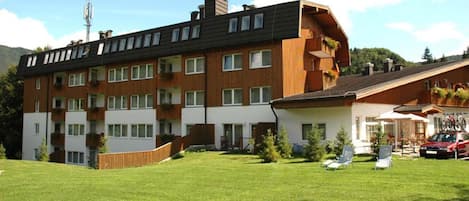 Un edificio residencial de varios pisos con balcones, un patio cubierto de césped y un coche estacionado afuera.