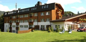 Un immeuble résidentiel à plusieurs étages, doté de balcons, d’une cour verdoyante et d’une voiture garée à l’extérieur.