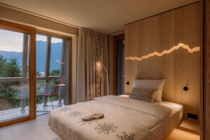 A bedroom with a large bed, a view of mountains, a balcony with a chair, and wooden paneling. - Bohinj (Bohinj)