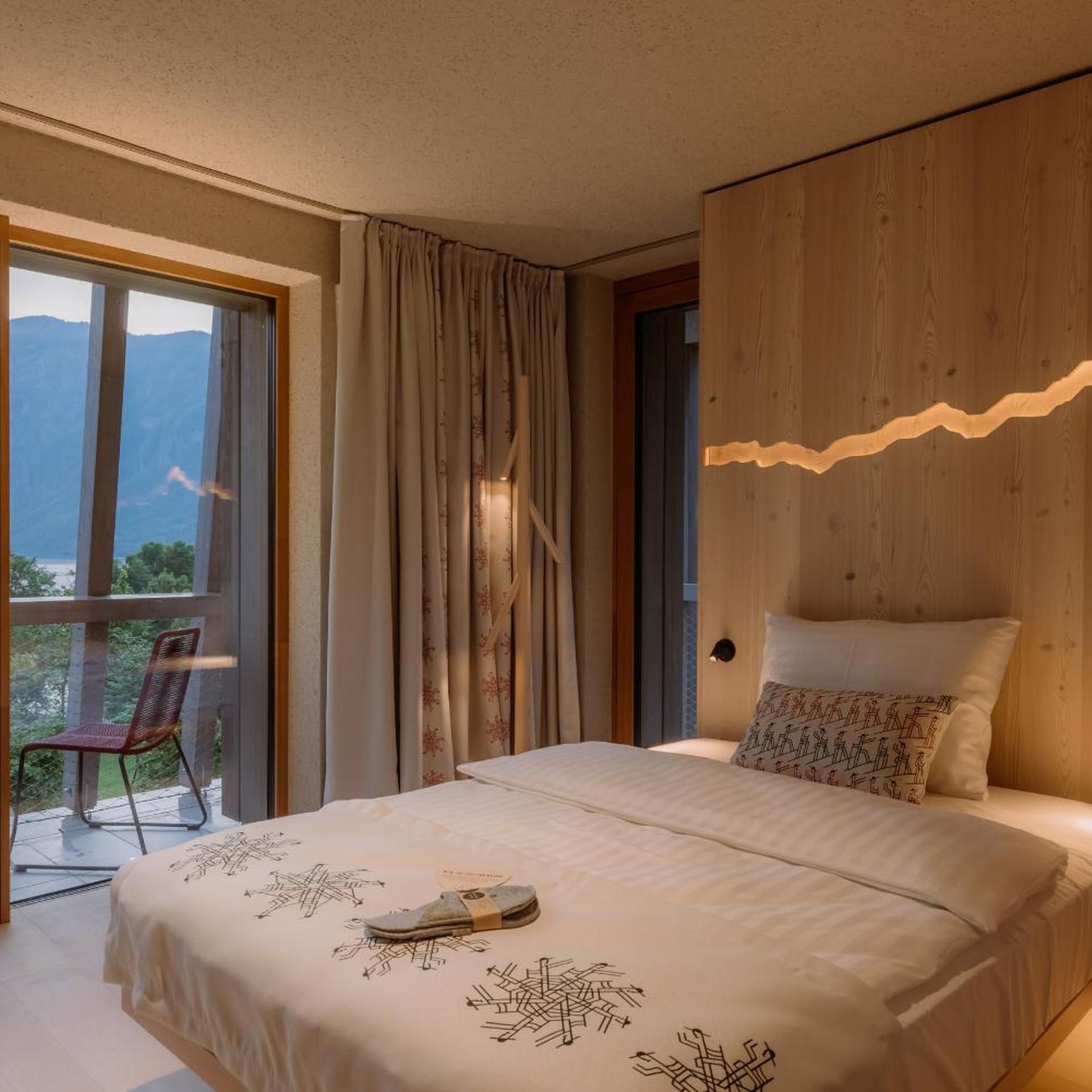 Une chambre avec un grand lit, une vue sur les montagnes par la fenêtre et un mur d’accent en bois.