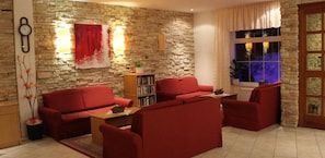 A living room with a stone wall, red sofas, a bookshelf, and a clock.