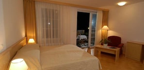 Ein Hotelzimmer mit Bett, Schreibtisch, Stuhl, Lampe und Blick ins Freie.