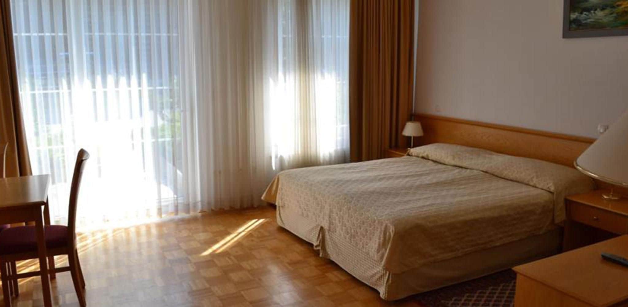 Une chambre d’hôtel avec un lit, un bureau, une chaise et une lampe.