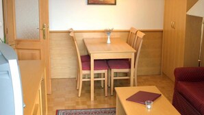A compact room with a wooden dining table, two chairs, a small table with a book and glass, a red sofa, a lamp, and a painting on the wall. - Bohinj (Bohinj)