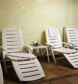 Ein Zimmer mit drei weißen Lounge-Sesseln, einem kleinen Tisch mit Kerze und einer Wand mit Muster.
