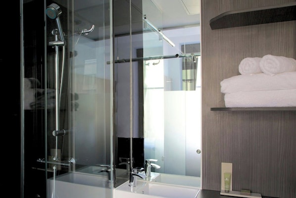 Une salle de bain moderne avec une douche à parois de verre, un lavabo blanc et une étagère où sont soigneusement pliées des serviettes.