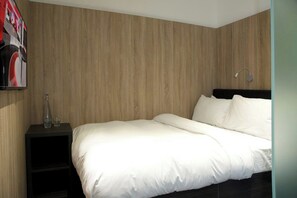 A bedroom with a wooden wall, a bed with white bedding, a nightstand with a bottle and glasses, and a wall-mounted light. - Z Hotel Glasgow (Glasgow)