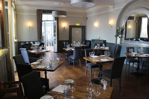 A restaurant with wooden tables and chairs, a large mirror, and a stone archway. - Bell Hotel (Sandwich)