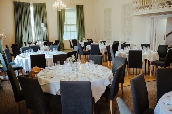 A dining area with round tables set for multiple guests, featuring white tablecloths and dark chairs. - Bell Hotel (Sandwich)