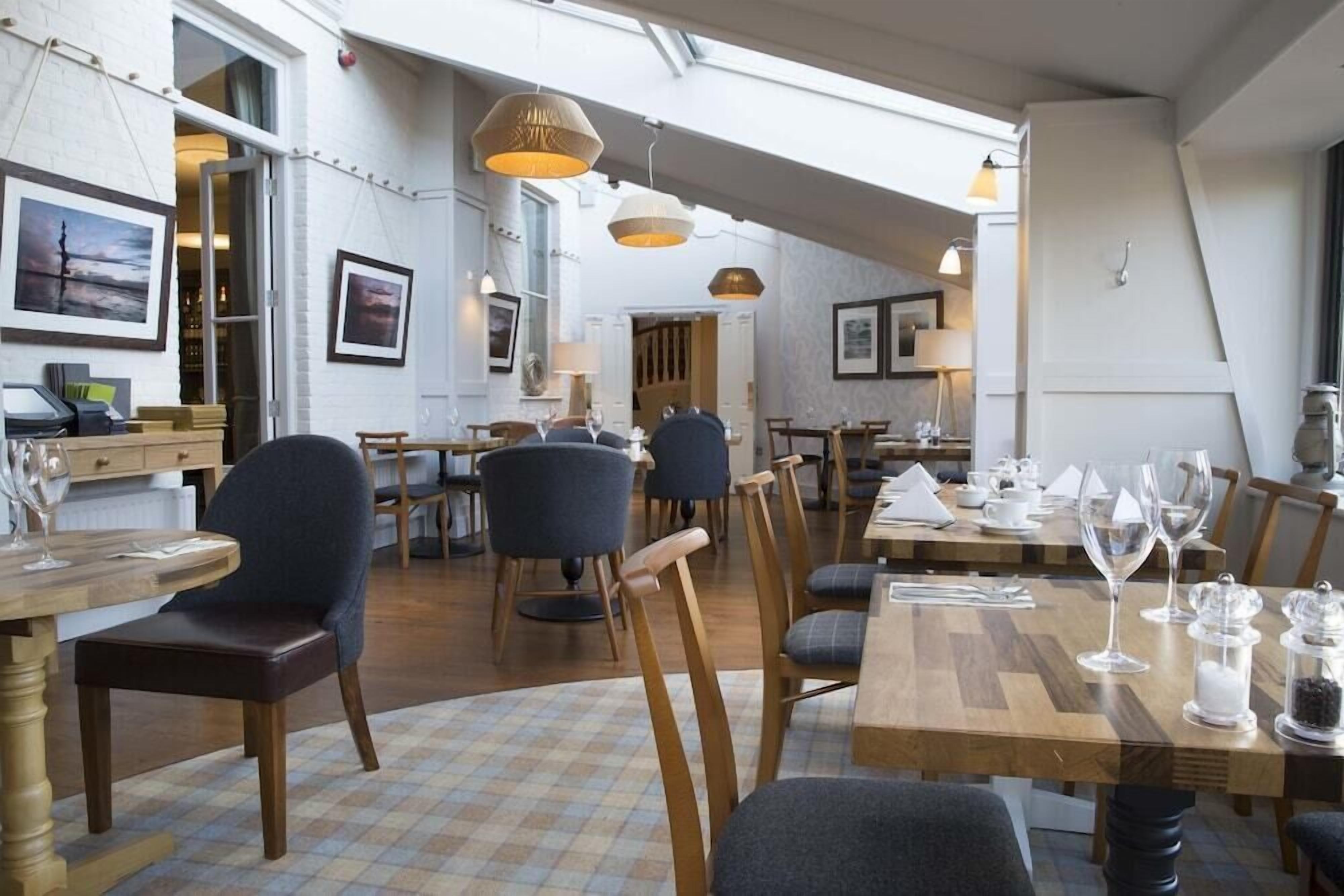 A spacious dining area with multiple tables and chairs, framed artwork on the walls, and pendant lighting.