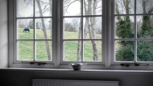 A room with a large window overlooking a grassy field and trees. - The Hurtwood Inn Hotel (Guildford)