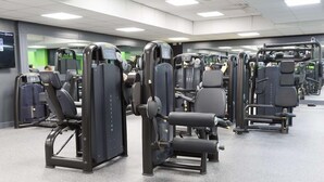 Ein Fitnessstudio mit verschiedenen Trainingsgeräten, darunter Gewichtbänke und Cardiogeräte.