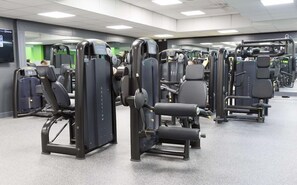 Ein Fitnessstudio mit verschiedenen Trainingsgeräten, darunter Gewichtbänke und Cardiogeräte.