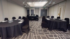 Ein Konferenzraum mit runden Tischen, Stühlen und einem gemusterten Teppich.
