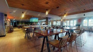 Ein geräumiges Restaurant mit Holzbalkendecke und moderner Beleuchtung, ausgestattet mit mehreren Esstischen und Stühlen.