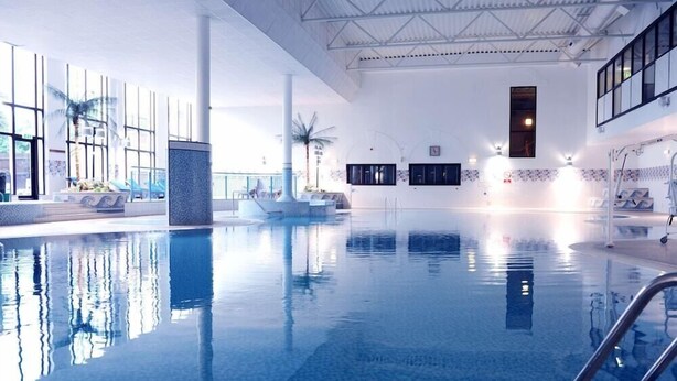 Ein heller, überdachter Pool mit klarem Wasser, gefliestem Boden und modernem architektonischen Design, das durch große Fenster und hohe Decken gekennzeichnet ist.
