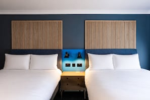 Habitació doble amb dos llits, una taula de nit, dues làmpades penjades a la paret i una paret decorativa blava.