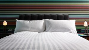 Ein Bett mit gestreifter Bettwäsche, ein Kopfteil mit schwarzen Kissen und zwei Nachttischlampen.