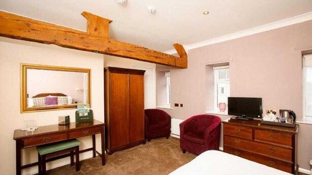 A bedroom with a wooden ceiling beam, a desk with a mirror, two red chairs, a dresser, and a television. - The Izaak Walton Country House Hotel (Ashbourne)