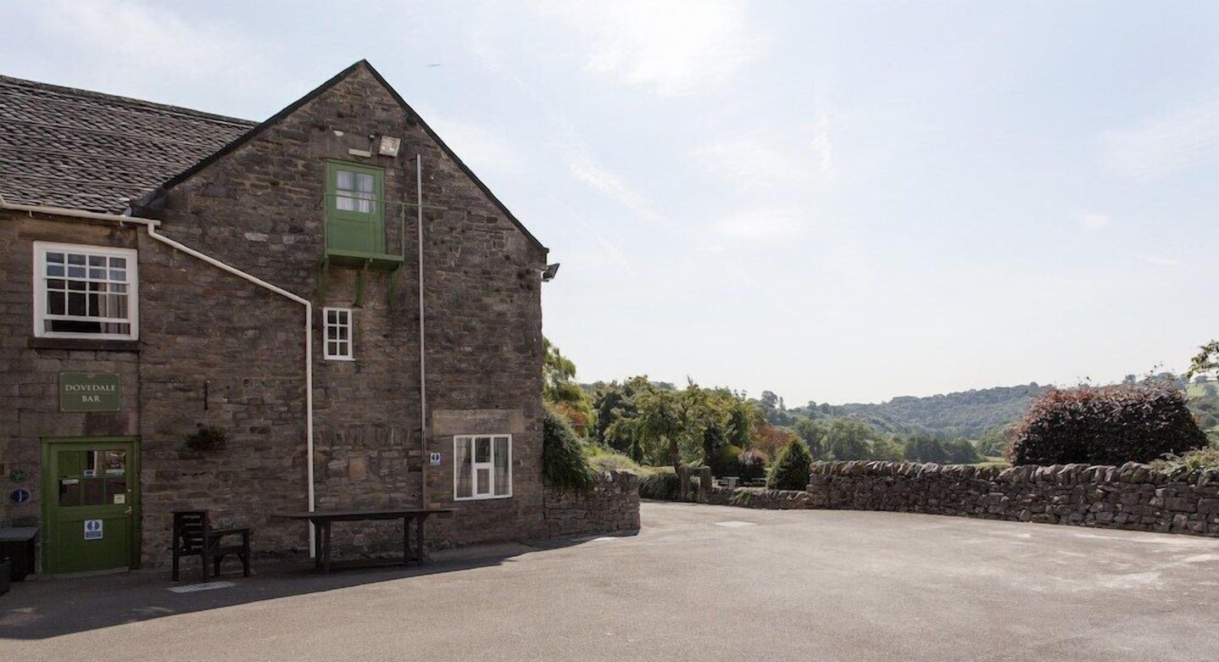 A stone building with a green door labeled "Dovetailed Bar" and a small outdoor seating area.