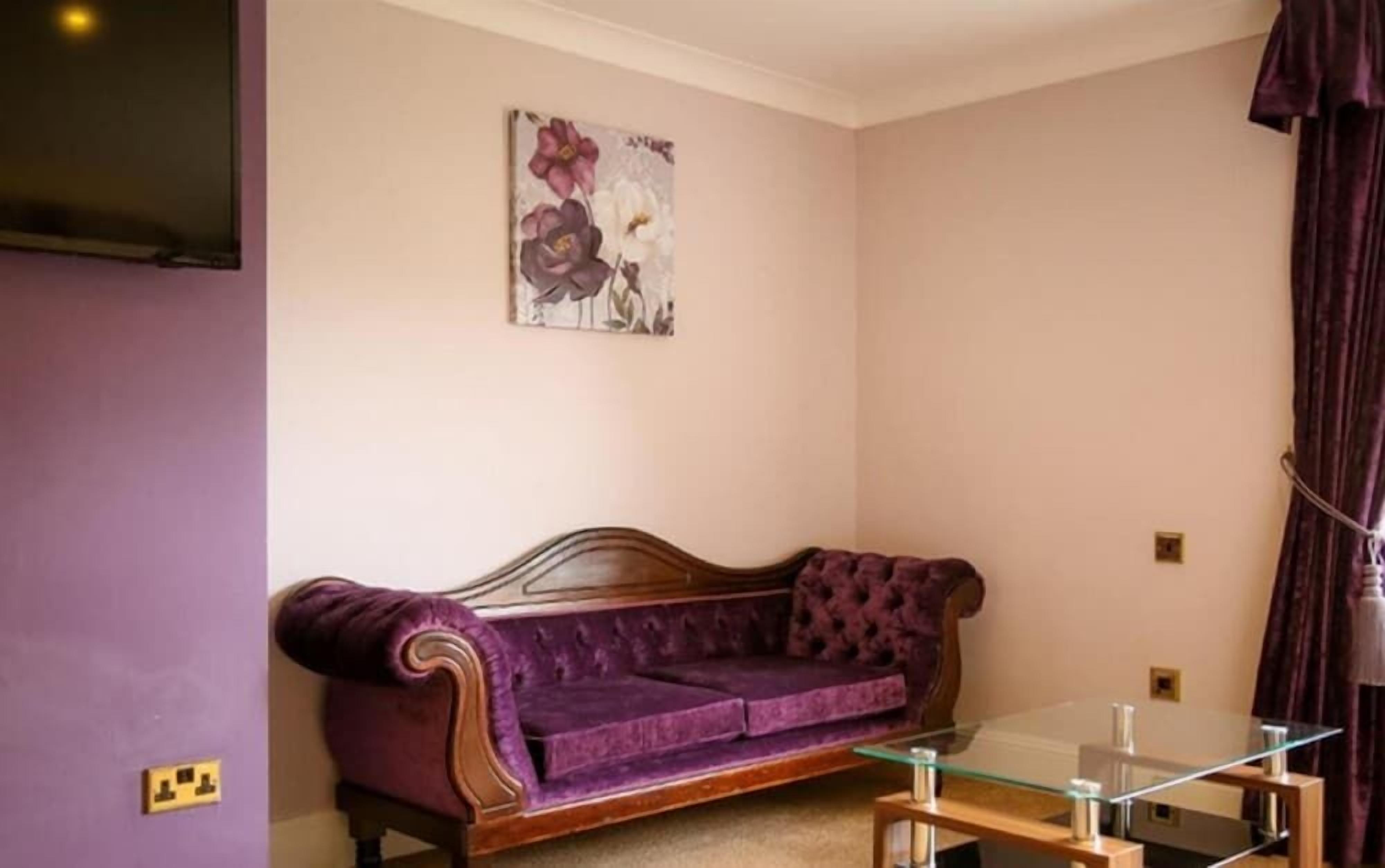 A purple sofa, a glass coffee table, and a wall-mounted painting in a room with light-colored walls.