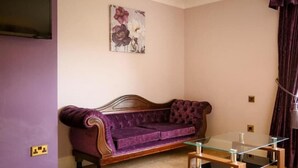 A purple sofa, a glass coffee table, and a wall-mounted painting in a room with light-colored walls. - The Izaak Walton Country House Hotel (Ashbourne)