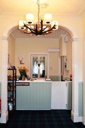 A reception area with a chandelier, a reception desk, and a mirror. - Atholl House Hotel (Dunvegan)