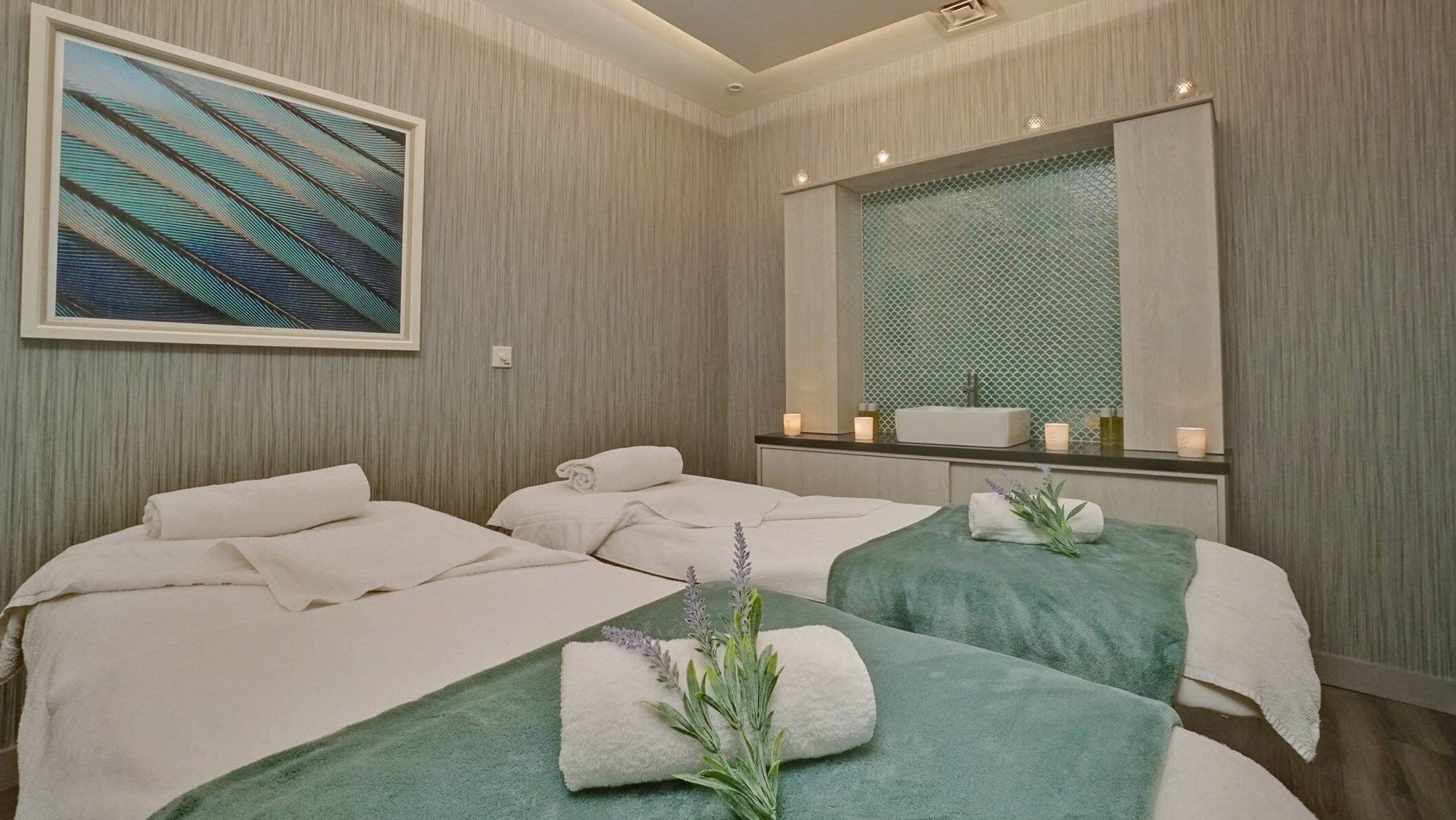 Ein Hotelzimmer mit zwei Betten, einem großen Spiegel, einem Wandbild und einer kleinen Badezimmerecke mit Waschbecken und Kerzen.