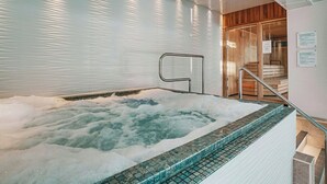 A hot tub with a tiled edge, a metal handrail, and a wooden door leading to a sauna area. - Wrightington Hotel And Country Club (Wigan)
