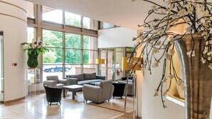 A spacious lobby with large windows, a seating area with sofas and armchairs, and a decorative plant arrangement. - Wrightington Hotel And Country Club (Wigan)