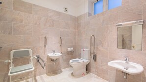 Ein modernes Badezimmer mit einer rollstuhlgerechten Sitzbank, Toilette, Waschbecken und Dusche.