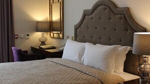 Ein Hotelzimmer mit einem großen Bett, einem Nachttisch mit Lampe, einem Sessel und einem Spiegel an der Wand.
