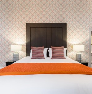 Une chambre d’hôtel avec un grand lit, deux oreillers, une tête de lit sombre et un papier peint à motifs.