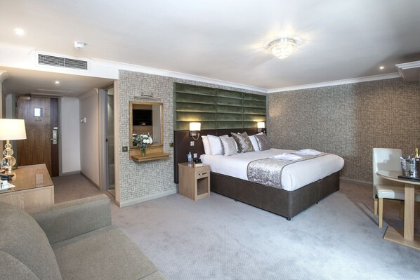 A modern hotel room with a large bed, a bedside table, a chair, a desk, and a mirror. - The Vale Golf Club (Pontyclun)