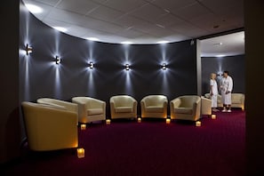 Um espaço de spa com seis cadeiras bege, um tapete vermelho e luminárias fixadas na parede.