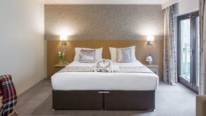 A hotel room with a large bed, two bedside lamps, a brick-patterned headboard, and a view of the outdoors through a large window.