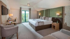 A hotel room with a large bed, two armchairs, a small table, and a view of the outdoors.