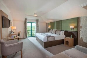 Une chambre d’hôtel avec un grand lit, deux fauteuils, une petite table et une vue sur l’extérieur.