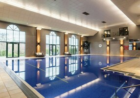 Una amplia piscina cubierta con paredes de vidrio transparente, una zona de recepción y un balcón.
