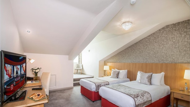 A hotel room with two beds, a TV, a desk with a laptop, and a small table with pastries.
