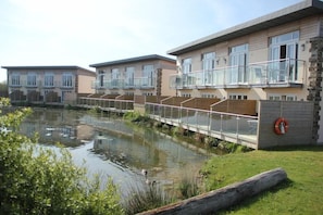 A modern residential building with a glass balcony, a small water body in front, and a grassy area. - Retallack Resort And Spa (St. Columb Major)