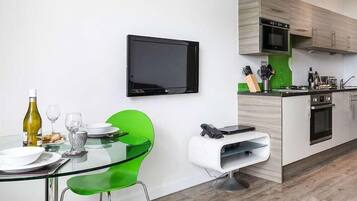 Una cocina moderna con televisor de pantalla plana, una mesa de comedor con sillas verdes y una pequeña isla con horno integrado.