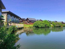A lakeside residential area with modern houses, a wooden dock, and lush greenery.