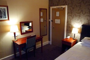 Hotellihuone, jossa on sänky, kaksi yöpöytää, työpöytä tuolilla, peili ja kaksi lamppua.