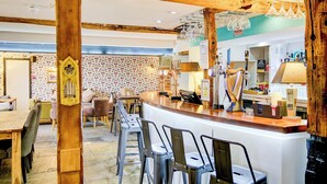 Una zona de bar con vigas de madera, taburetes y una barra con vasos y botellas.